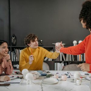 Three people discussing Human Resource Management at a table; one passes a document to another.