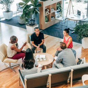 Five employees discuss "Employee Motivation" in a modern office with wooden floors and potted plants.