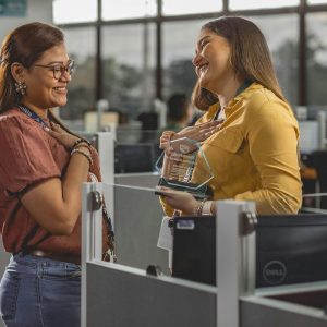 Two women smiling in an office; one proudly holds a glass plaque that reads "Employee Recognition.