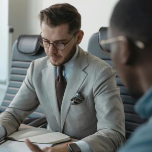 Two men at a table discuss Employee Recruitment, one writing in a notebook while the other listens attentively.