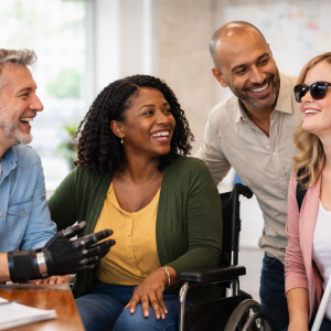 Four adults indoors, including a woman in a wheelchair and another with a white cane, smiling together.