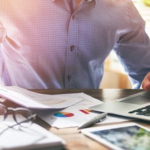 Person in blue at desk with “Administrative Office Procedures” book and office supplies.