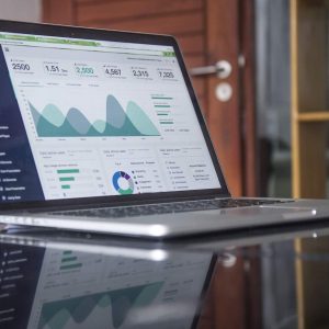 Laptop on glass table displays “Budgets and Financial Reports - Self Study” dashboard with charts.