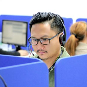 Man wearing headset at computer reviews “Call Center Training - Self Study” near blue office dividers.
