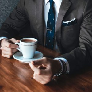 Man in suit at table reads “Coaching Salespeople - Self Study” and holds coffee cup.