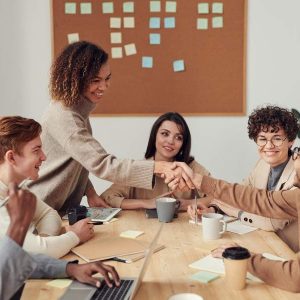 Five professionals shaking hands and smiling, collaborating in a business writing course setting.