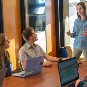 Woman leads Employee Onboarding - Self Study with two colleagues at laptops in a modern office.