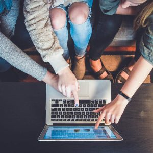 Three people gathered around a laptop, discussing “Internet Marketing Fundamentals - Self Study” materials.