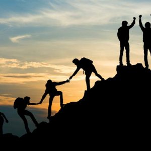 Group helps each other climb a rocky hill at sunset; “Life Coaching Essentials” text visible.