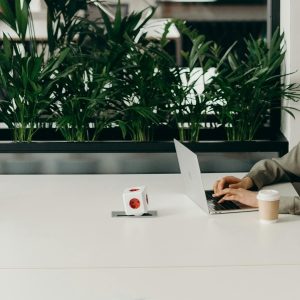 Woman at white table in office with laptop, coffee, and plants studying Microsoft Outlook 2024.