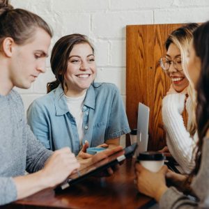 Four people chatting at a table with coffee cups and a tablet in a relaxed, casual environment.