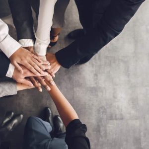 Eight professionals huddle, showing teamwork; text: Motivating Your Sales Team - Self Study.