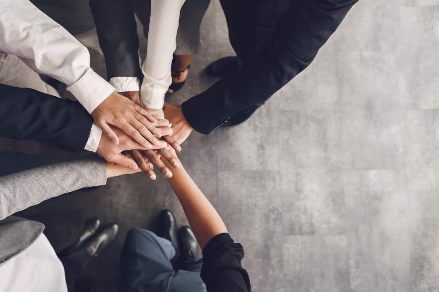 Eight professionals huddle, showing teamwork; text: Motivating Your Sales Team - Self Study.