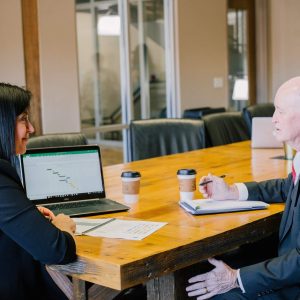 Two professionals with laptops and coffee discuss “Multi-Level Marketing - Self Study” at a table.