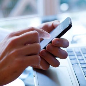 MLearning Essentials - Self Study open on smartphone, user’s hand on laptop keyboard.